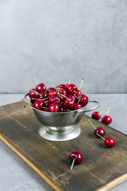 Gümüş bir kevgir/elek bir ahşap tahta üzerinde taze, tatlı kiraz. Gri arka planı.