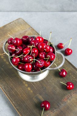 Gümüş bir kevgir/elek bir ahşap tahta üzerinde taze, tatlı kiraz. Gri arka planı.