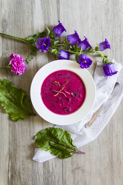 Pancar, pancar çorbası bırakır. Beyaz tabak, ahşap arka plan, çiçekler.