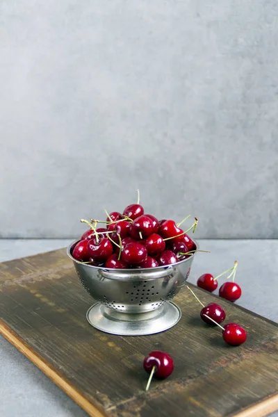 Gümüş bir kevgir/elek bir ahşap tahta üzerinde taze, tatlı kiraz. Gri arka planı.