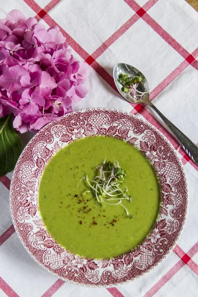 Vintage plaka üzerinde yeşil bezelye çorbası. Beyaz masa örtüsü, pembe ortanca.