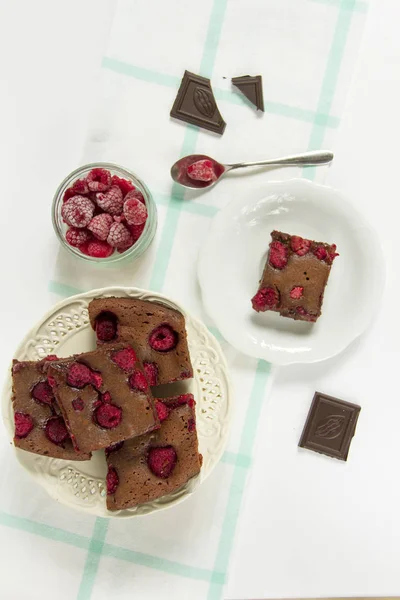 Brownie with raspberries. White plates, white background. Fruits and chocolate.