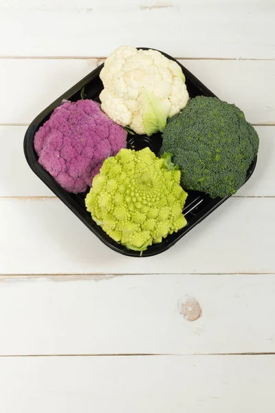 Taze organik beyaz ve mor karnabahar, brokoli, romanesco. Ahşap masa, kase, ahşap kesme tahtası.