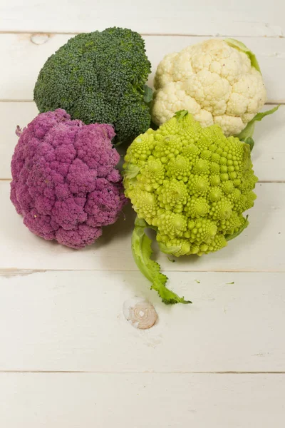 Taze organik beyaz ve mor karnabahar, brokoli, romanesco. Ahşap masa, kase, ahşap kesme tahtası.