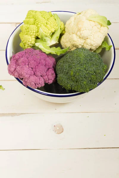 Taze organik beyaz ve mor karnabahar, brokoli, romanesco. Ahşap masa, kase, ahşap kesme tahtası.