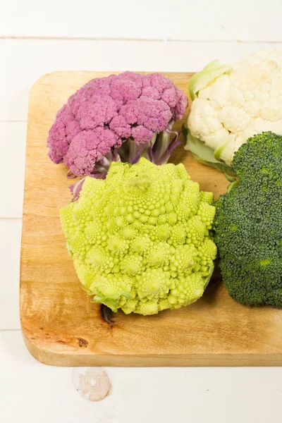 Taze organik beyaz ve mor karnabahar, brokoli, romanesco. Ahşap masa, kase, ahşap kesme tahtası.