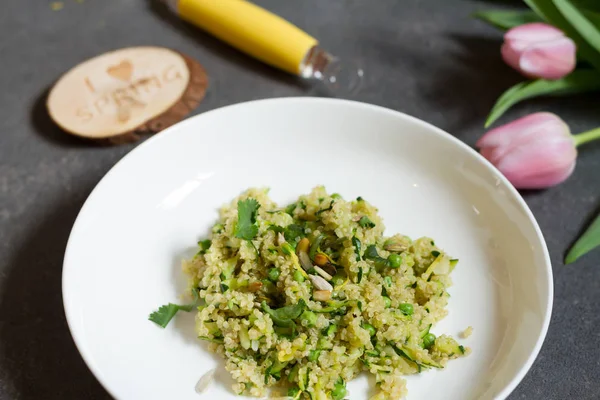 Kabak ve yeşil bezelye ile Quinoa. Gri arka plan, beyaz tabak ve laleler.