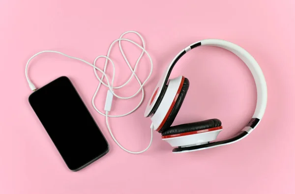 Smartphone e cuffie su sfondo rosa. Melodia giovanile . — Foto Stock