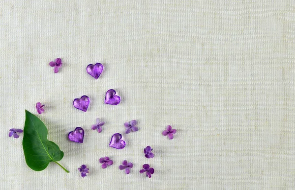 violet heart, lilac flowers and leaves on fabric background.