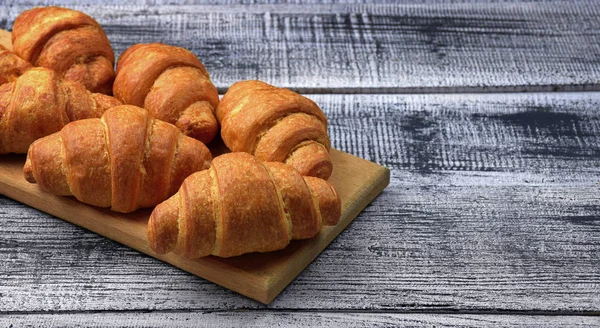 Fresh croissants on an old wooden table in a rural setting. — Stock Photo, Image