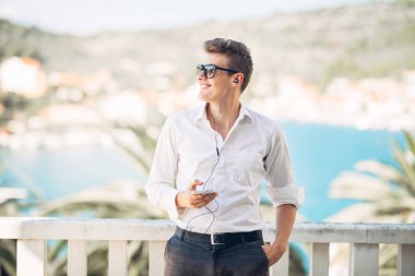 Denizin panoramik manzaralı lüks resort Hotel'de konaklamanın tadını yakışıklı delikanlı. Kazanılan bir tropikal tatil onun smartphone seçenekleri kullanarak gülümseyen iş adamı. İş seyahat. Dış kaynak