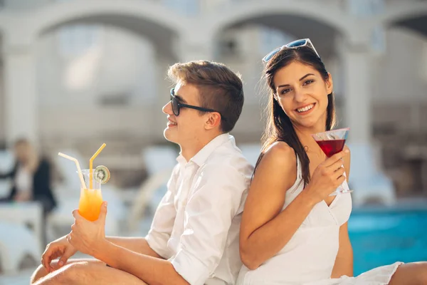 stock image Youbg cheerful loving couple having cocktails by the pool on summer vacation.Romantic evening in luxury resort.Celebrating love ,engagement,anniversary.Enjoying time together.Relaxing with your better half