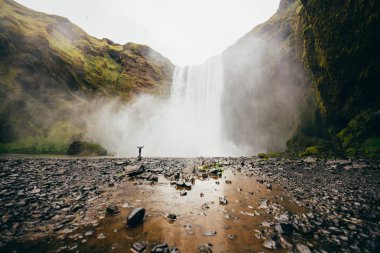 Turist Iceland.Man güçlü doğa ile karşılaştırıldığında güneyinde meşhur Skogafoss Şelalesi önünde duruyor. Küçük insan doğa kavram. İnsan ve doğa bağlantı kavramı. Seyahat, kamp, keşfetmek