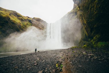 Turist Iceland.Man güçlü doğa ile karşılaştırıldığında güneyinde meşhur Skogafoss Şelalesi önünde duruyor. Küçük insan doğa kavram. İnsan ve doğa bağlantı kavramı. Seyahat, kamp, keşfetmek