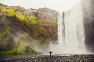 Turist Iceland.Man güçlü doğa ile karşılaştırıldığında güneyinde meşhur Skogafoss Şelalesi önünde duruyor. Küçük insan doğa kavram. İnsan ve doğa bağlantı kavramı. Seyahat, kamp, keşfetmek