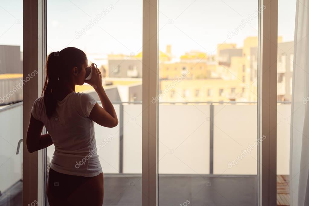 Sleepy woman stretching,drinking a coffee to wake up early in the monday morning sunrise.Starting your day.Wellbeing.Positive energy,productivity,happiness,enjoyment concept.Morning ritual