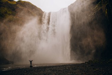 Turist Iceland.Man güçlü doğa ile karşılaştırıldığında güneyinde meşhur Skogafoss Şelalesi önünde duruyor. Küçük insan doğa kavram. İnsan ve doğa bağlantı kavramı. Seyahat, kamp, keşfetmek