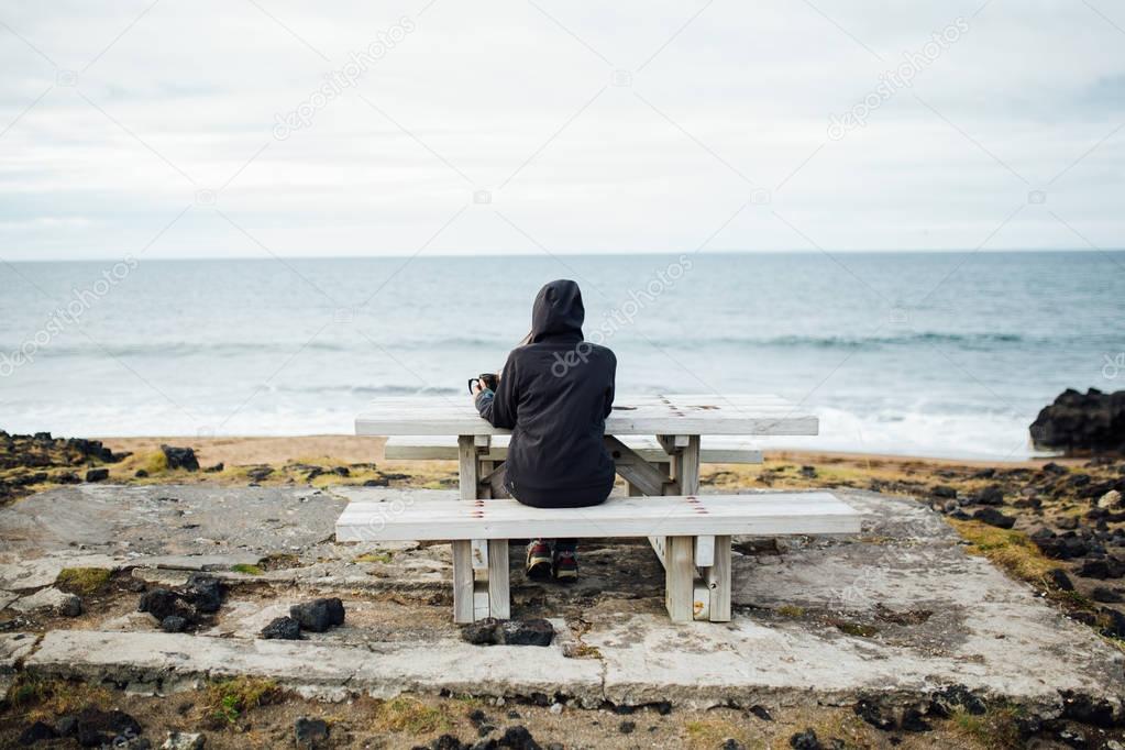 Isolated nostalgic woman siting on a bench by the sea.Pensive female thinking by the calming ocean waves.Pensive person struggling with mental problems,depression and anxiety.Rethinking and reflecting
