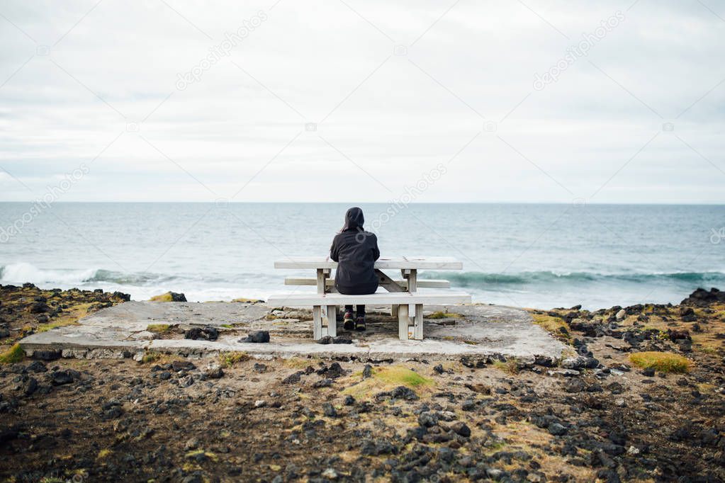 Isolated nostalgic woman siting on a bench by the sea.Pensive female thinking by the calming ocean waves.Pensive person struggling with mental problems,depression and anxiety.Rethinking and reflecting