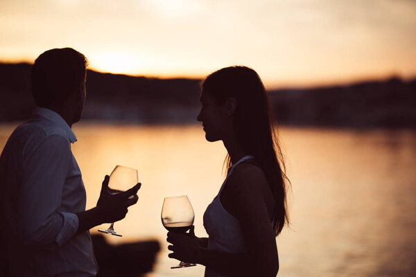 Two young people enjoying a glass of red wine in the sunset on the seaside.Healthy glass od homemade red wine,Mediterranean culture.Warm climates,seaside living couple.Seaside vacation experience