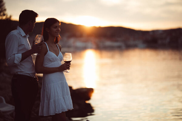 Two young people enjoying a glass of red wine in the sunset on the seaside.Healthy glass od homemade red wine,Mediterranean culture.Warm climates,seaside living couple.Seaside vacation experience