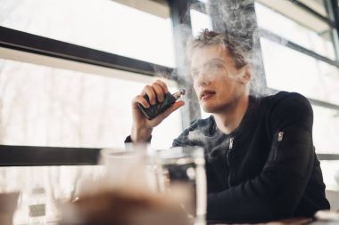 Vaping kapalı kamusal alanda genç adam. Kafede elektronik sigara içiyorum. Nikotin bağımlılığı. Sigara, eski alışkanlık çıkmak için bir yol. Vaping aroma, e-sigara yerlerde sigara kullanan kentsel adam izin verilmiyor