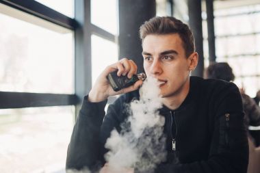 Vaping kapalı kamusal alanda genç adam. Kafede elektronik sigara içiyorum. Nikotin bağımlılığı. Sigara, eski alışkanlık çıkmak için bir yol. Vaping aroma, e-sigara yerlerde sigara kullanan kentsel adam izin verilmiyor