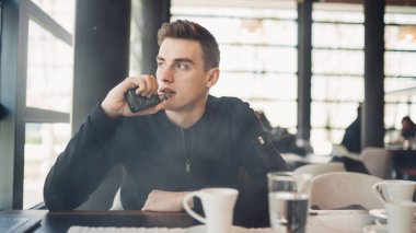 Vaping kapalı kamusal alanda genç adam. Kafede elektronik sigara içiyorum. Nikotin bağımlılığı. Sigara, eski alışkanlık çıkmak için bir yol. Vaping aroma, e-sigara yerlerde sigara kullanan kentsel adam izin verilmiyor