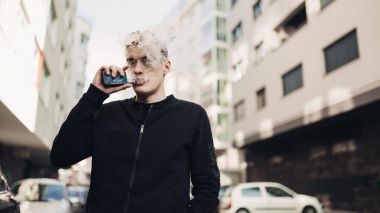 Halka açık yerlerde sigara elektronik sigara kullanan genç adam. Kısıtlama, Sigara yasağı sigara. Vaping aygıt ile aromalı sıvı kullanarak. E-suyu vaping. Sigara alışkanlığı, nikotin bağımlısı, tütün endüstrisi