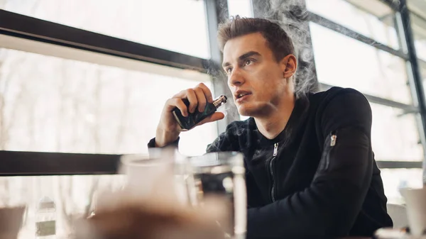 Vaping kapalı kamusal alanda genç adam. Kafede elektronik sigara içiyorum. Nikotin bağımlılığı. Sigara, eski alışkanlık çıkmak için bir yol. Vaping aroma, e-sigara yerlerde sigara kullanan kentsel adam izin verilmiyor