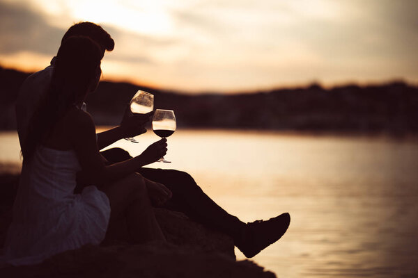 Romantic couple drinking wine at sunset at a pier on a seaside.Romance.Two people having a romantic evening with a glass of wine near the sea.Enjoying company.Celebrating anniversary.Honeymoon