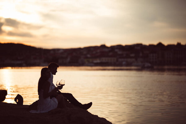 Romantic couple drinking wine at sunset at a pier on a seaside.Romance.Two people having a romantic evening with a glass of wine near the sea.Enjoying company.Celebrating anniversary.Honeymoon