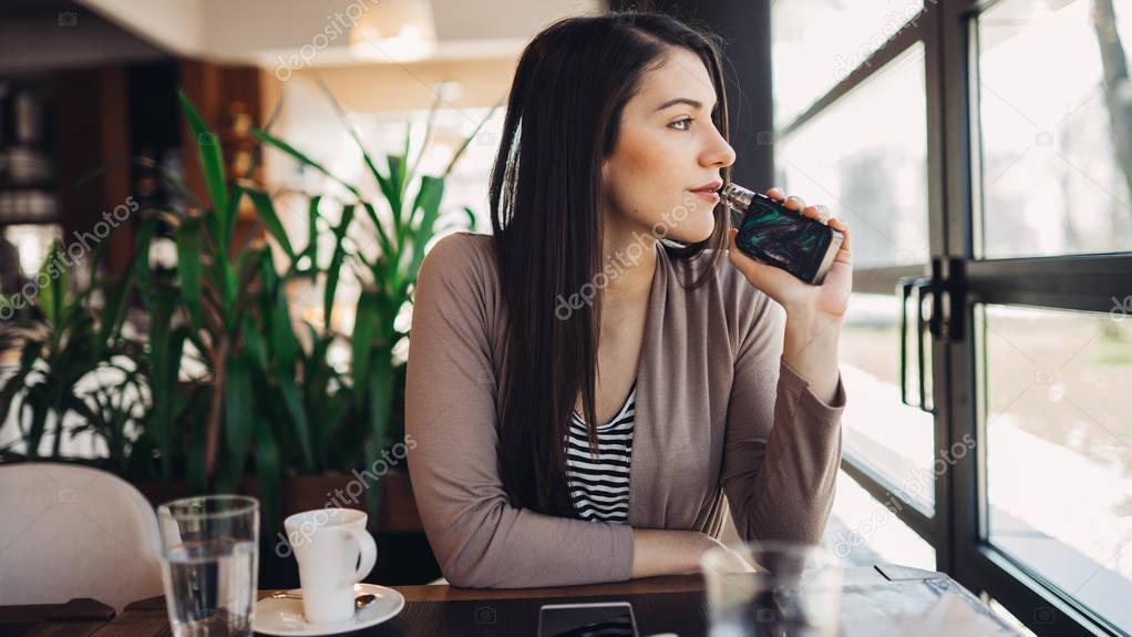 Young woman using electronic cigarette to smoke in public places.Smoke restriction,smoking ban.Using vaping device with flavoured liquid.E-juice vaping.Smoking habit,nicotine addict,tobacco industry