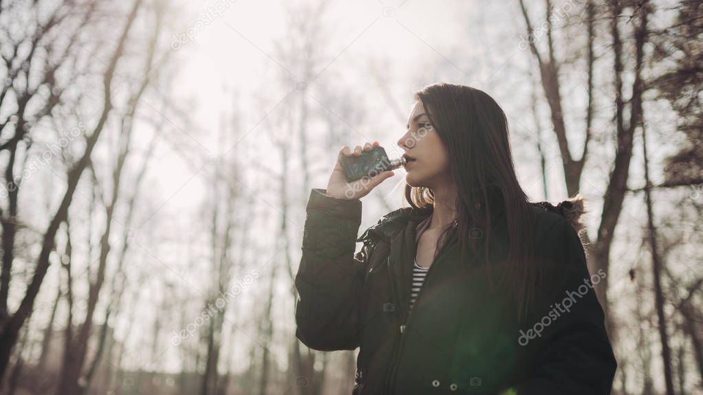 Young woman using electronic cigarette to smoke in public places.Smoke restriction,smoking ban.Using vaping device with flavoured liquid.E-juice vaping.Smoking habit,nicotine addict,tobacco industry