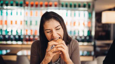 Young woman eating fatty hamburger.Craving fast food.Enjoying guilty pleasure,eating junk food.Satisfied expression.Breaking diet rules,giving up diet.Unhealthy imbalanced nutrition calorie intake. clipart