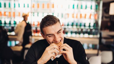 Genç adam yeme yağlı hamburger. Özlem lokanta. Abur cubur yeme suçlu zevk zevk. Memnun ifade. Son dakika diyet kuralları, diyet kadar vererek. Sağlıksız dengesiz beslenme kalori alımını.