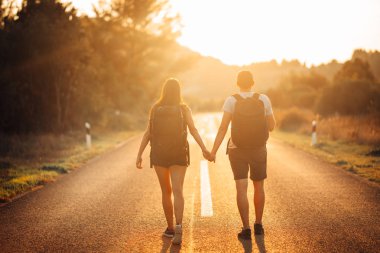 Genç, sırt çantalı, maceraperest bir çift yolda otostop çekiyor. Hayat macerası, seyahat tarzı. Düşük bütçeli seyahatler.