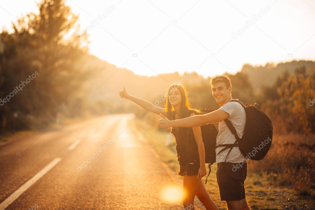 Young backpacking adventurous couple hitchhiking on the road.Stopping transportation.Travel lifestyle.Low budget traveling.Adventurous active vacations.Hitchhiking tourism concept.Backpackers together