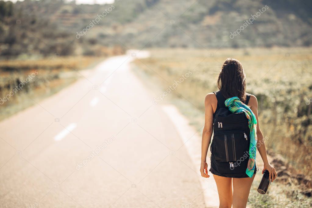 Young backpacking adventurous woman hitchhiking on the road.Traveling backpacks volume,packing essentials.Travel lifestyle.Low budget traveling.Adventurous active vacations.Hitchhiking tourism concept