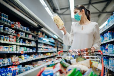 Koruyucu yüz maskesi olan genç insan marketten erzak / erzak alıyor. Coronavirus covid-19 salgını nedeniyle salgın için karantina hazırlığı. Çürütülemez gıda gereksinimlerinin seçilmesi