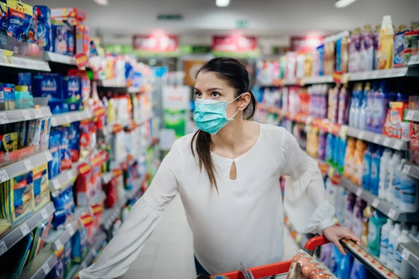 Virüs salgınına karşı koruyucu maske takan kadın karantinaya alındı. Süpermarketteki raflarda doğru ürünleri buluyor. Hijyen, temizlik ve dezenfeksiyon ürünleri..