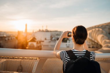 Akıllı telefonuyla fotoğraf çeken genç bir kadın, şehir manzarası açısından gün batımının tadını çıkarıyor. Sevilla, Endülüs, İspanya 'da inanılmaz deneyimi olan bir turist. Güneşin ve panoramın tadını çıkarıyor. Seyahat fotoğrafçılığı.