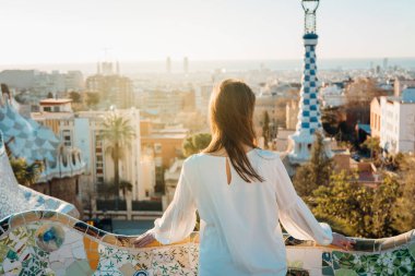 Genç bayan turist tatilini Barselona, Katalonya, İspanya 'da geçiriyor. Avrupa' ya seyahat ediyor, Parc Guell UNESCO 'nun ünlü tarihi eserlerini ziyaret ediyor. Girişte panoramik manzara. Barselona' da en iyi gün doğumu.