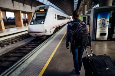 Çantalı ve sırt çantalı bir kadın turist tren / metro istasyonuna gidiyor. Ulaşım seçenekleri, varış noktasına ulaşma. Bagajla tren yolculuğunun tadını çıkarıyorum. Bir trene biniyorum. Yer bağlantıları.