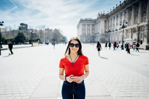 Happy woman tourist in front of Cathedral Santa Maria la Real de La Almudena in Madrid,Spain.Tourist using vacation sim card and tarrif to stay connected.Browsing on mobile phone abroad.Roaming