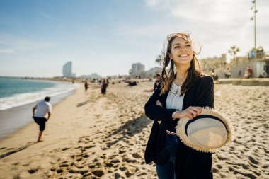 Kaygısız kadın turist sahilde keyif çatıyor. Hasır şapkalı neşeli bir kadın bahar mevsiminde kumsalda saçlarını dalgalandırarak yürüyor. İspanya 'nın Barceloneta plajında kadın gezgin.