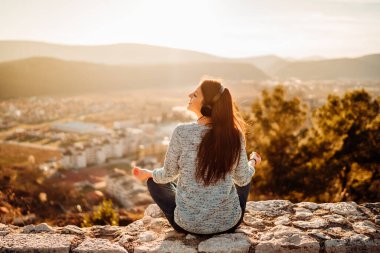 İyimser genç bir kadın kulaklıkla müzik dinliyor, günbatımında doğanın tadını çıkarıyor. Müzikal terapi. Doğanın bir günü. Farkındalık meditasyona rehberlik etti..
