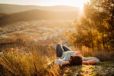 İyimser genç bir kadın kulaklıkla müzik dinliyor, günbatımında doğanın tadını çıkarıyor. Müzikal terapi. Doğanın bir günü. Farkındalık meditasyona rehberlik etti..
