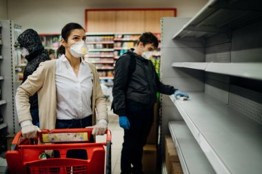 Maske takan ve eldiven giyen insanlar marketten tükenmiş ürünlerle erzak / erzak alıyorlar. Coronavirus covid-19 salgını nedeniyle yiyecek stokları azalıyor ve stok yapıyorlar..