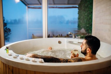 Jakuzide bir bardak şarapla evde dinlenen bir adam. Banyo jakuzisinde spa günü. Boş zaman etkinliği. Kişisel hijyen rutini.
